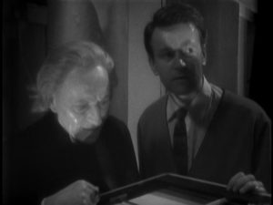 The Doctor and Ian, in a shadowy room, examine a piece of scientific equipment. Ian looks concerned.